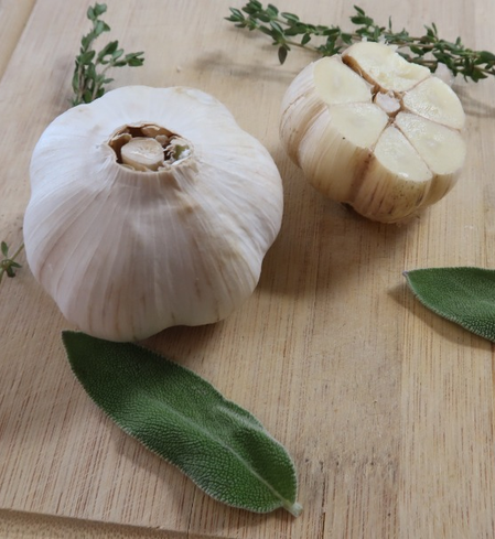 Fresh garlic bulbs on a wooden cutting board, accompanied by sage leaves and thyme sprigs, showcasing the ingredients for flavorful cooking.